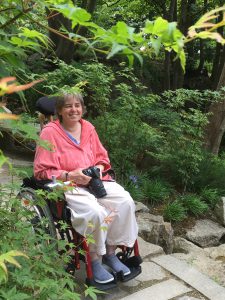 Corina Duyn, with camera in hand, seated in wheelchair - birds make her smile